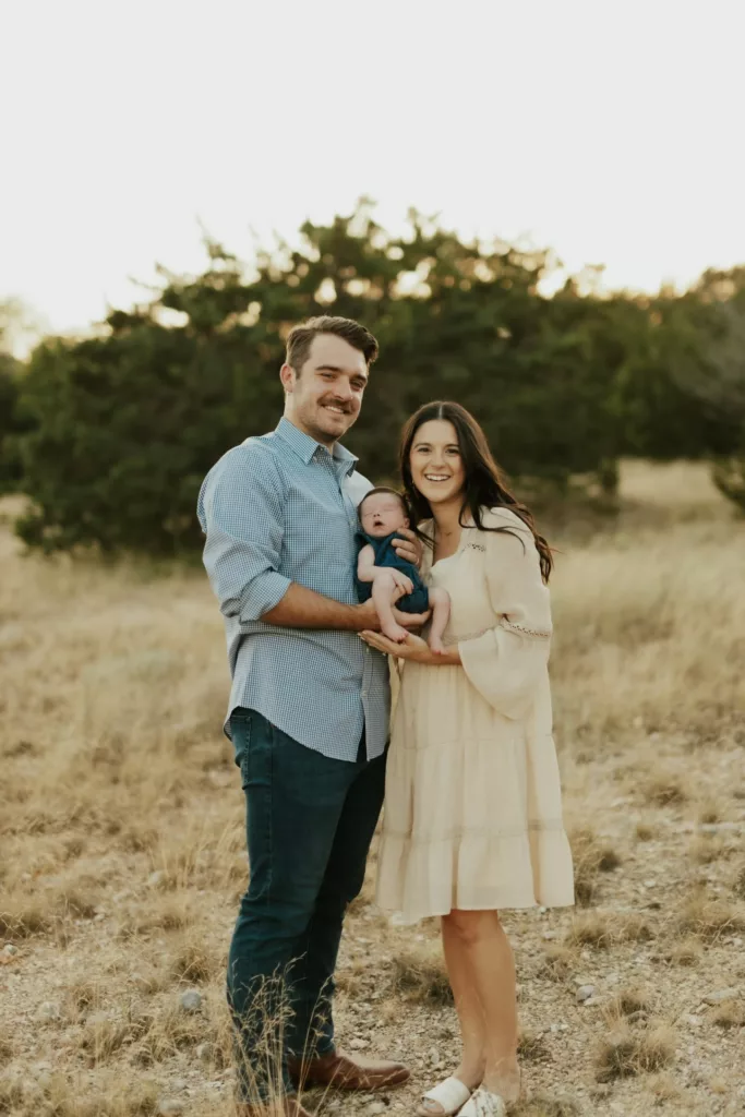 Auggie, alongside his wife and baby, posing in a vast grassland area, capturing a moment of familial bliss and the expansive beauty of nature, with the tall grasses and open skies enveloping them.